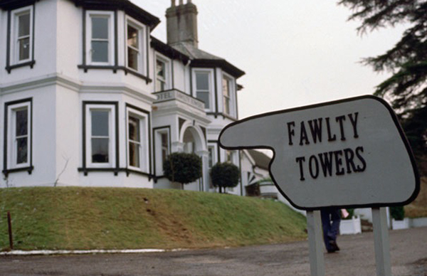 Image of Fawlty Towers from the 1970s television series of the same name. Hotel in background with a sign in the shape of a pointing finger .